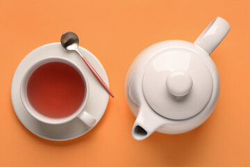 Obraz na płótnie Canvas Ceramic teapot and cup of tea on orange background