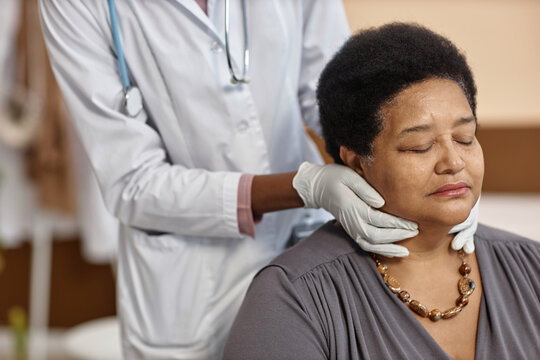 Unrecognizable doctor checking lymph nodes of senior African American female patient sitting with closed eyes during check up in hospital - Powered by Adobe