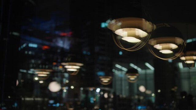Blurred interior of the restaurant with bright lighting and people partying reflecting in the window over night cityscape