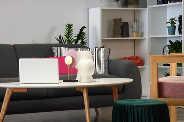 Coffee table with modern laptop and decorative vases in stylish living room