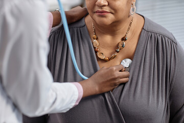 Cropped shot of unrecognizable female patient at check up in clinic with doctor pressing stethoscope to her chest - obrazy, fototapety, plakaty