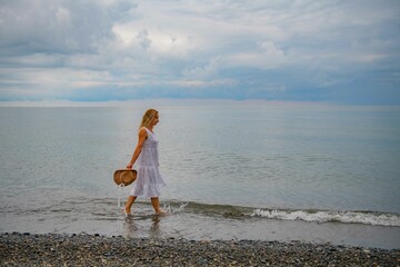 Fototapeta na wymiar Woman in a white dress walking on the seashore
