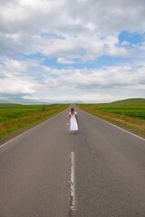 Fototapeta premium A girl in a white dress is walking along the road