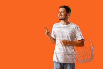 Young man with shopping basket pointing at something on orange background