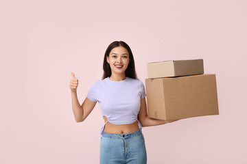 Pretty young woman with parcels showing thumb-up on pink background