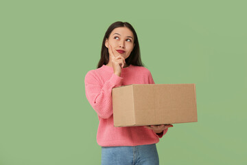Thoughtful young woman with parcel on green background