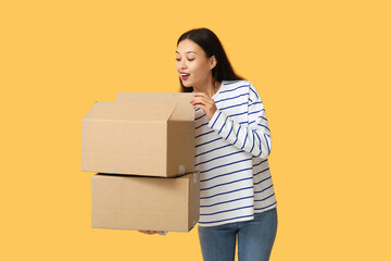 Surprised young woman with open parcel on yellow background
