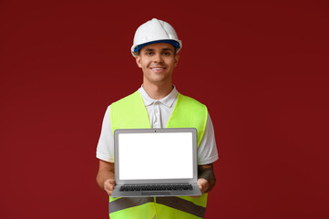 Young male engineer showing laptop with blank screen on red background