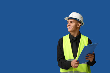 Young male engineer with clipboard on blue background