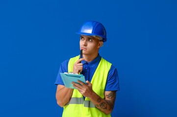 Thoughtful male engineer with clipboard on blue background