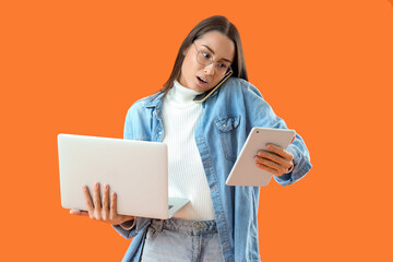 Female seller with laptop and tablet computer talking by mobile phone on orange background