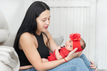 young latina mother holding her baby on her lap while looking at her with pride and love - obrazy, fototapety, plakaty