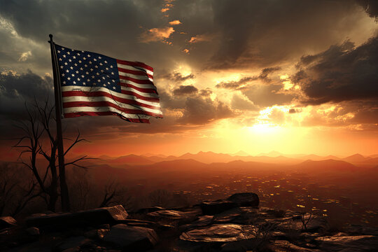 American flag waves on a mountaintop at sunset, with a barren tree nearby and a town below.