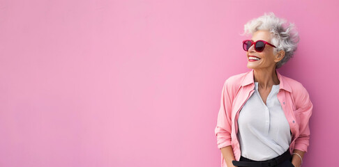 Happy smiling woman of senior old age standing on pink background wall. Modern elderly female - obrazy, fototapety, plakaty