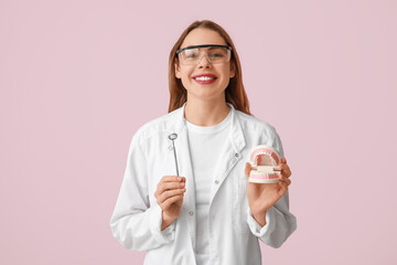 Female dentist with jaw model and dental mirror on pink background. World Dentist Day