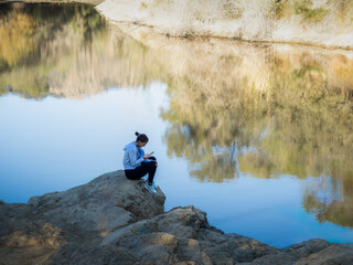 Solitary Woman on Lakeside Rock Engaged with Her Phone