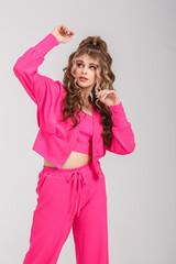 young girl in pink suit poses as doll on white background in studio