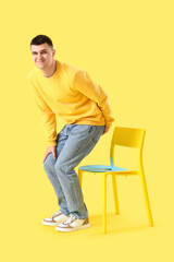 Naklejka premium Young man with hemorrhoids and paper thumbtack on chair against yellow background