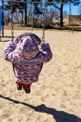 Back view of child wearing a parka on a swing in a children playground