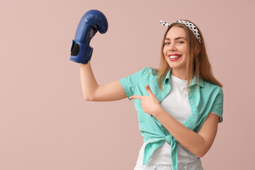 Happy young pin-up woman pointing at boxing glove on pink background