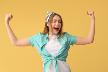 Happy young pin-up woman showing her muscles on yellow background