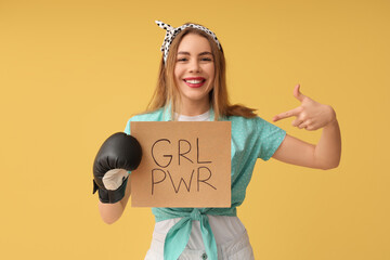 Happy young pin-up woman in boxing glove pointing at card with text GIRL POWER on yellow background
