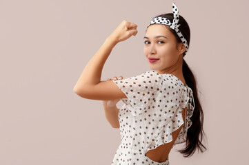 Beautiful young Asian pin-up woman showing her muscles on pink background