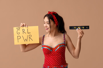 Beautiful young Asian pin-up woman holding spirit level and card with text GIRL POWER on brown...