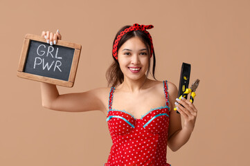 Beautiful young Asian pin-up woman holding chalkboard with text GIRL POWER, pliers and spirit level...