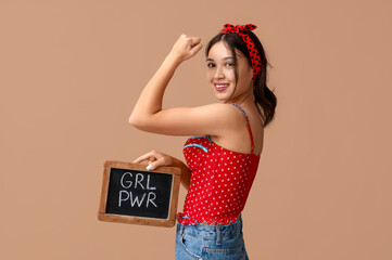Beautiful young Asian pin-up woman holding chalkboard with text GIRL POWER and showing her muscles...