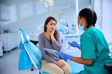 Young woman in pain talking to her dentist at dental clinic.