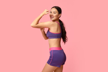 Fototapeta na wymiar Young woman in sportswear showing muscles on pink background