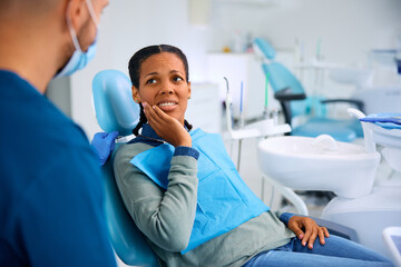 Black woman complaining about toothache during appointment at dentist's office.