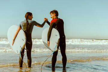 Two surfers greet each other by shaking hands before surfing on waves in ocean