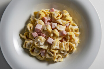 Top view of White soup bowl with tortellini with cream and ham