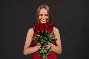 Portrait of attractive young woman is standing on black background with roses box in hands