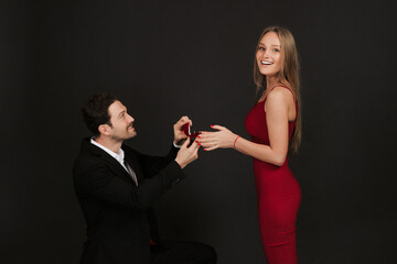 Beautiful romantic couple isolated on black background. A handsome man in a suit is proposing to his attractive young woman in a red dress. Couple in love. Happy Valentine