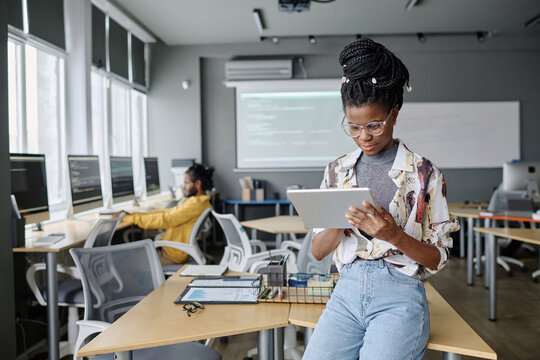 Young black engineer with braids typing on tablet, her male colleague working on background