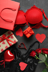 Shopping bag with sexy underwear, gift boxes and bouquet of roses on grunge black background. Valentine's Day celebration