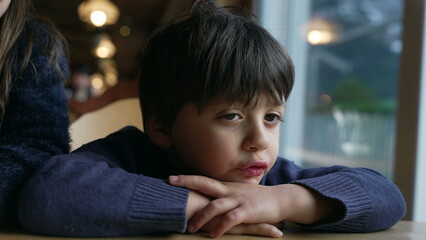 Bored small boy complaining, sulking child feeling annoyed leaning on restaurant table, closeup kid...