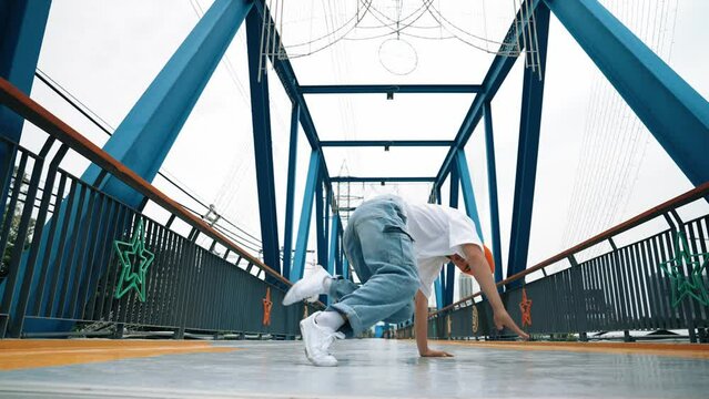 Professional break dancer perform street dance footstep at bridge. Asian hipster wear headphone while doing freeze pose. Break dancer, street dancer freestyle concept. Outdoor sport 2024. Sprightly.