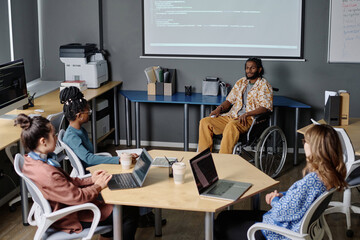 Indian man in wheelchair giving speech to his colleagues in office, code projected on digital board