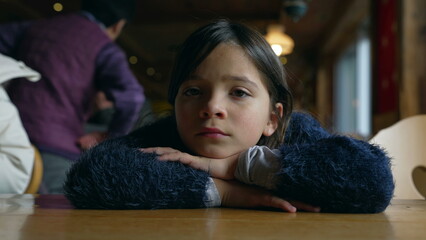 Closeup of 8 year old girl staring at camera with blank face expression, child daydreaming at diner