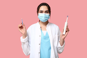 Young female dentist in mask with electric toothbrush and brush for cleaning braces on pink background