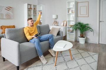 Young man playing video game on grey sofa in living room