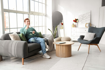 Young man with cup of coffee sitting on soft sofa in living room