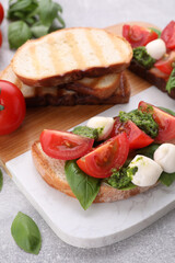 Fototapeta na wymiar Delicious Caprese sandwiches with mozzarella, tomatoes, basil and pesto sauce on light grey table