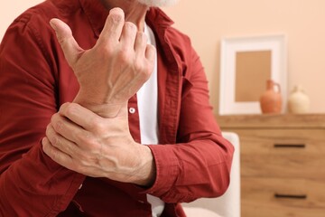 Senior man suffering from pain in his hand at home, closeup. Arthritis symptoms