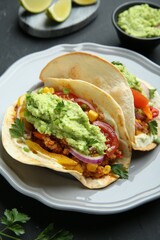 Delicious tacos with guacamole, meat and vegetables on black table, closeup