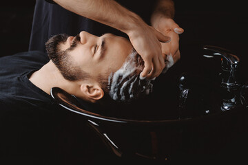Hairdresser use shampoo for washing hair of man in barbershop. Concept spa cosmetic for men